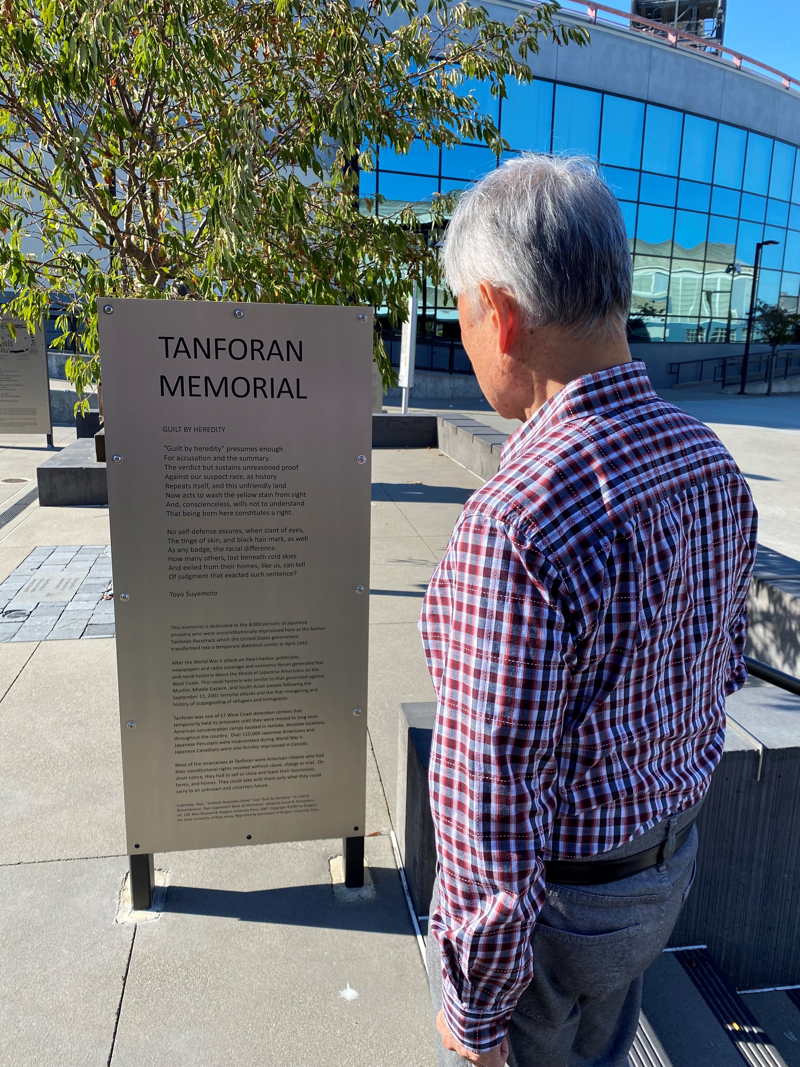 George Takei looking at metal sign describing Tanforan Memorial