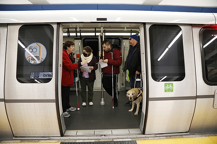 Blind and low vision riders congregate in front of an opened door in a out of service Fleet of the Future train