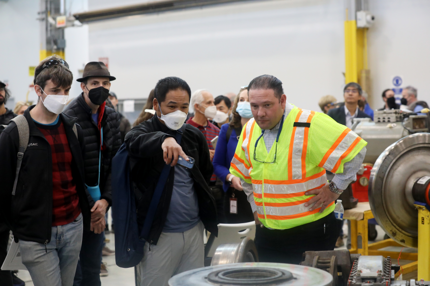 A BART employee in a yellow vest explains equipment to members of the public in the Hayward Maintenance Complex.