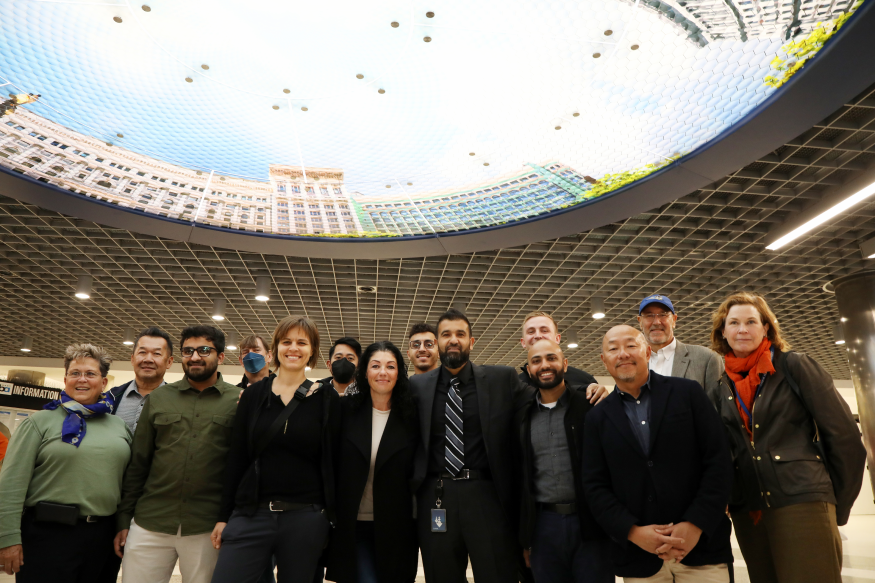 The team behind the Powell St. Modernization Program poses for a photo under “Elysium” by Stephen Galloway on Nov. 22, 2022.