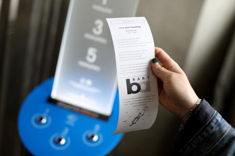 A hand holding a short story in front of a dispenser