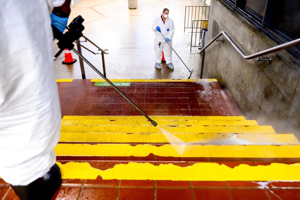 Dirt is blasted off stairs with the hot steam power washer, while a cleaner squeegees the water into a nearby drain.  