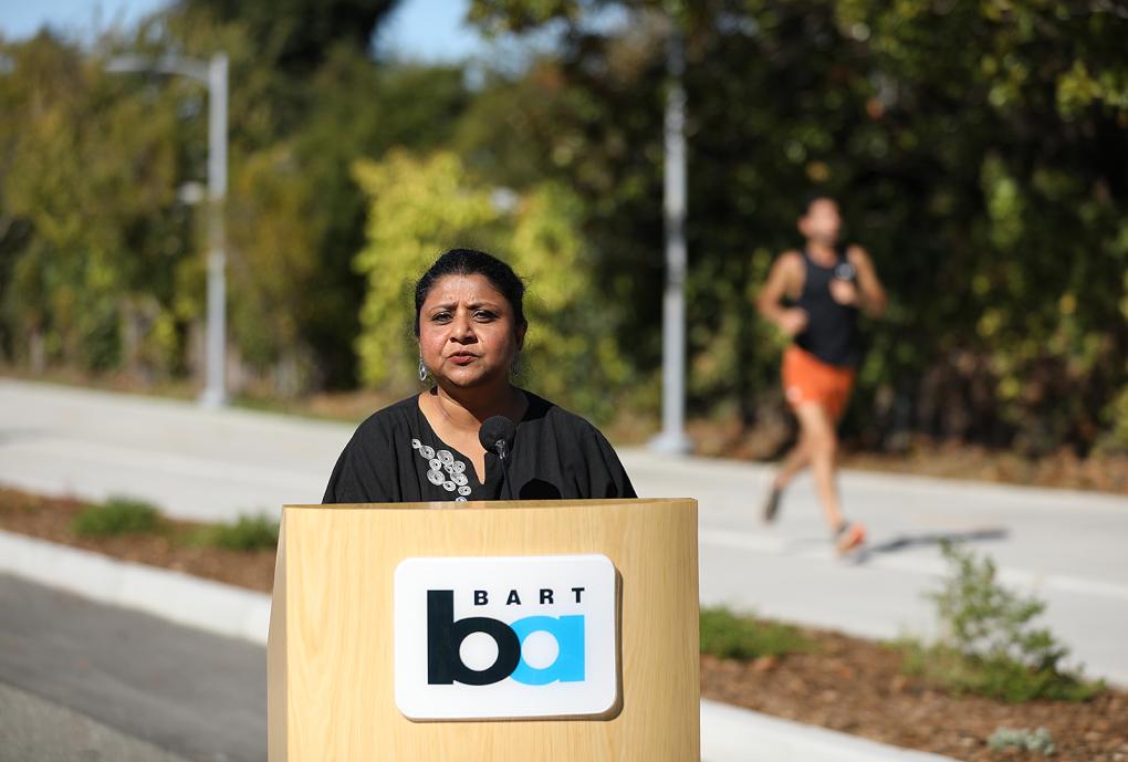 Director Barnali Ghosh speaks at the ribbon cutting at a podium with the BART logo