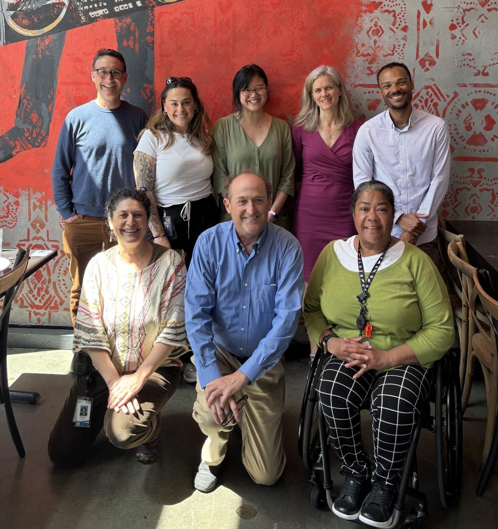 Bob is pictured kneeling with team members on either side and five people standing behind them against a colorful backdrop