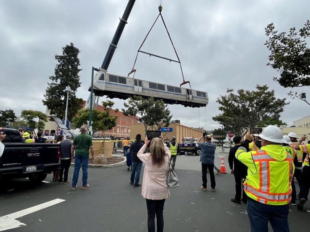 Legacy BART car on a crane with people watching