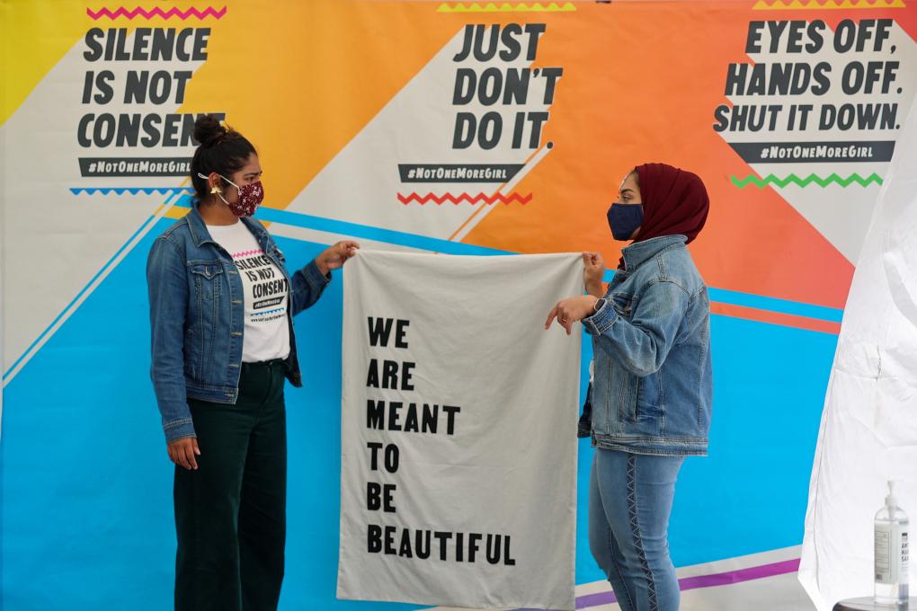 Organizers pose for a photo holding banner "We Are Meant to Be Beautiful" at Not One More Girl's Art Activation event.