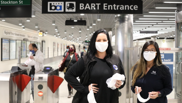 2 station agents in masks greeting riders