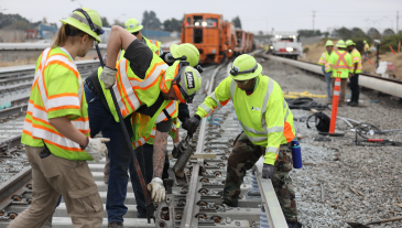 Track workers wearing yellow safety vests aligning track 